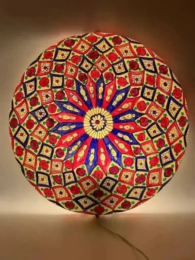 A vibrant hand-painted camel skin lamp with a symmetrical mandala design in red, blue, yellow, and green.