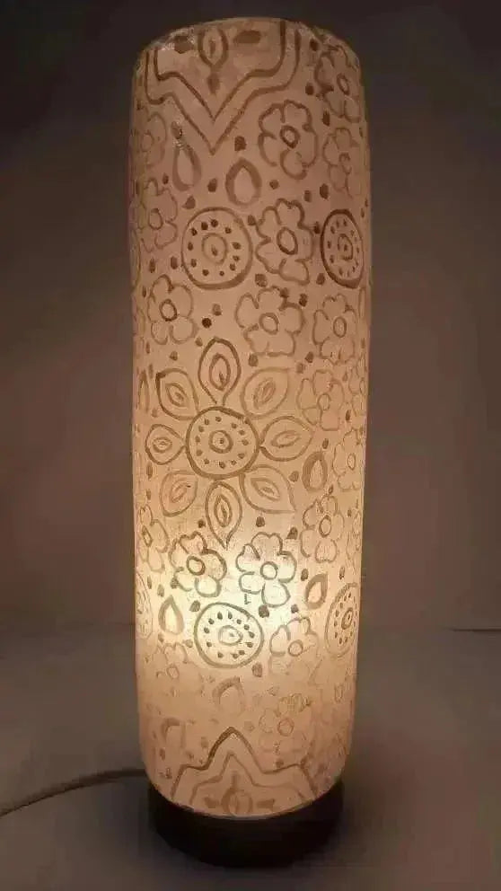 A cylindrical ceramic table lamp with intricate floral patterns emitting warm glow from the handcrafted glass shaped lamps collection.