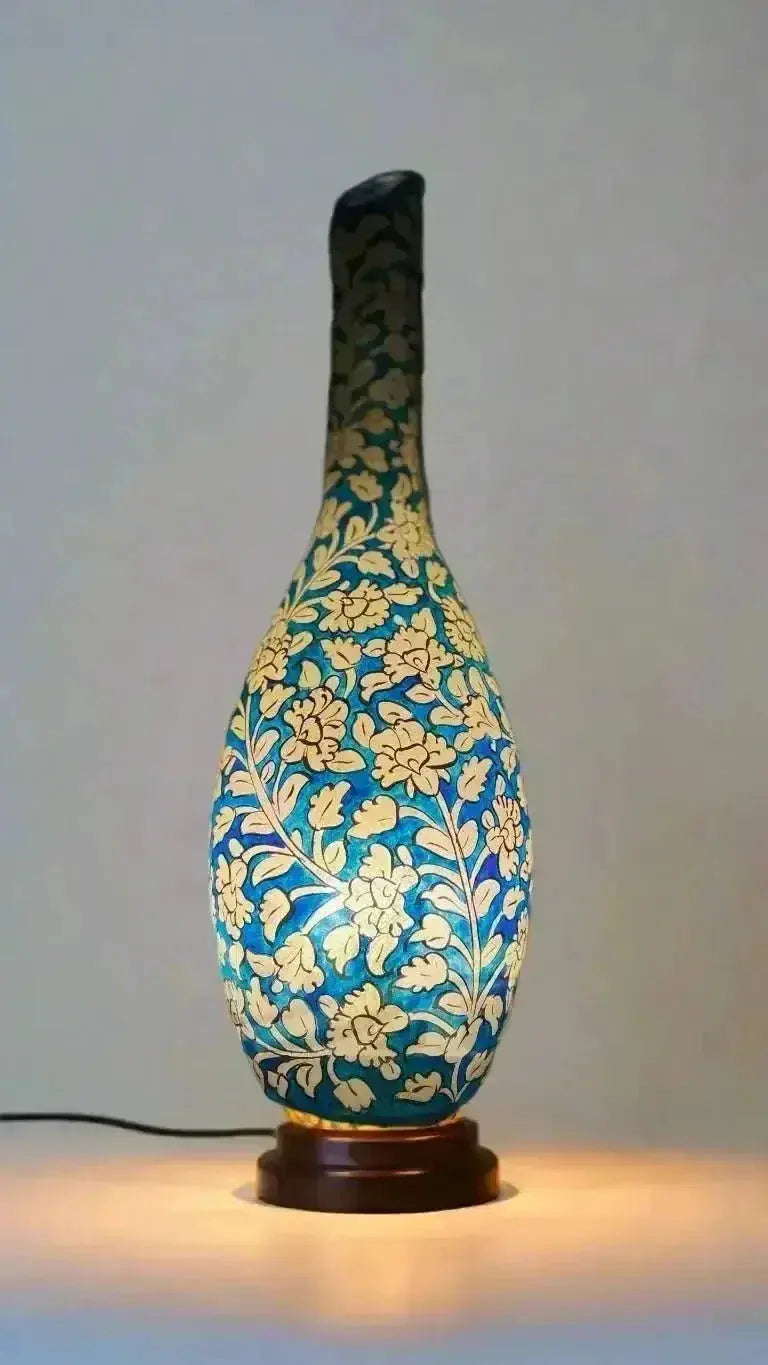 A blue ceramic surahi shape camel vase with intricate gold floral patterns and darkened neck on wooden base